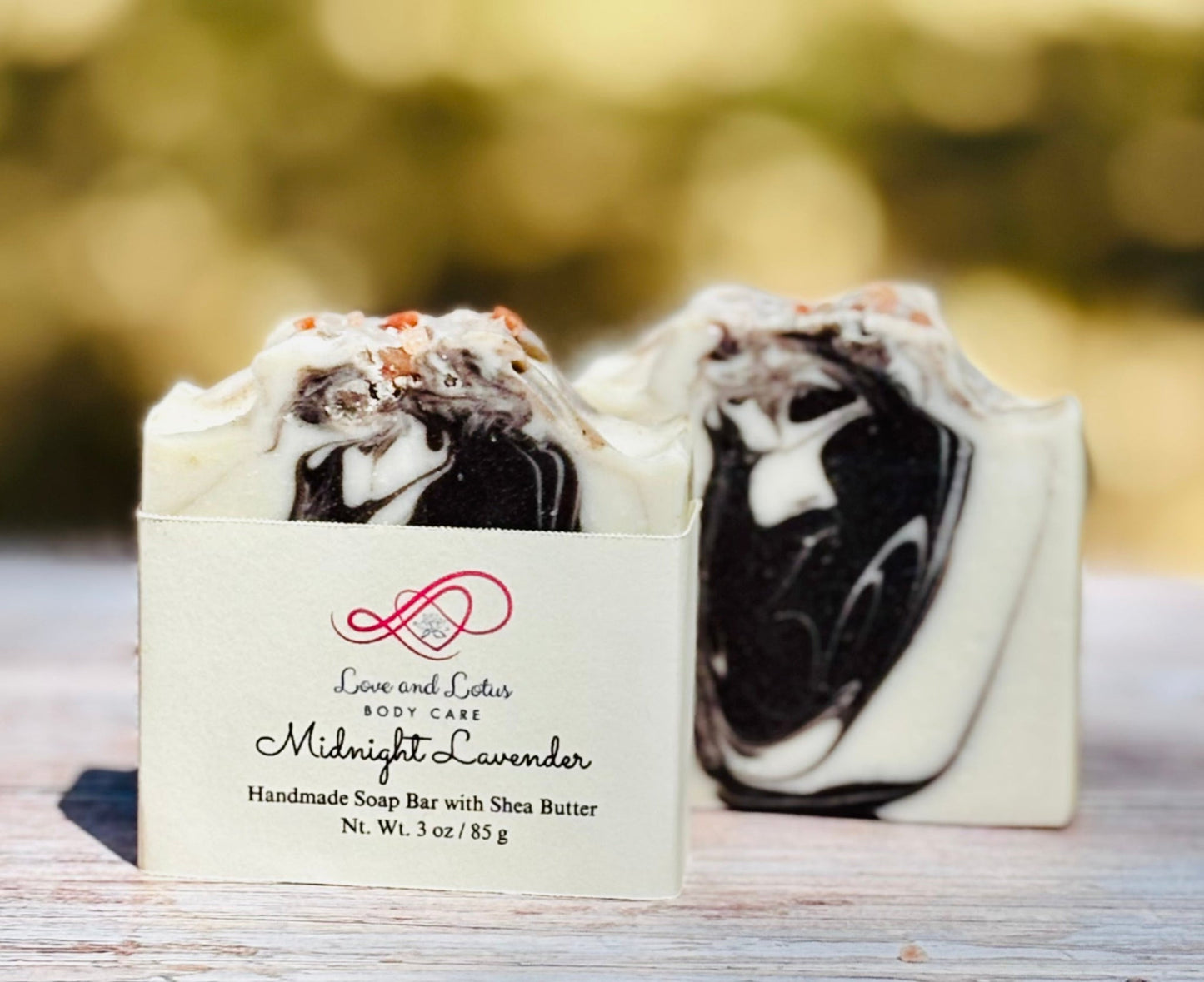 Black and white soap bar with a Love and Lotus Body Care label on a wooden surface.