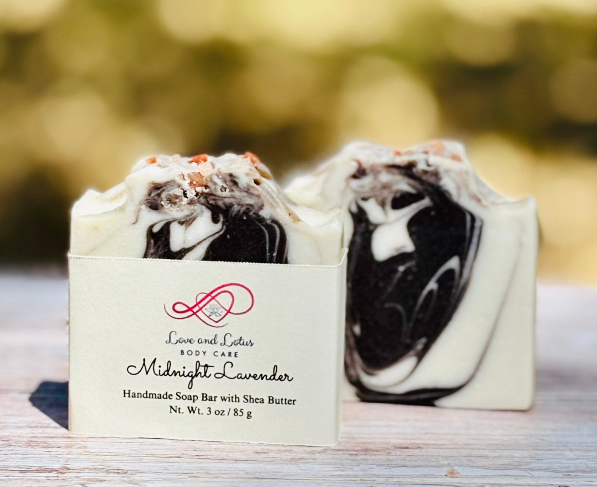 Black and white soap bar with a Love and Lotus Body Care label on a wooden surface.